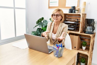 Middle age blonde woman smiling confident having video call at office