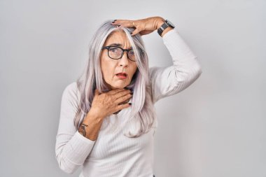 Middle age woman with grey hair standing over white background touching forehead for illness and fever, flu and cold, virus sick 