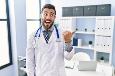 Doktor üniforması giyen yakışıklı İspanyol adam ve klinikte steteskop gülen surat ve baş parmağıyla yüzünü gösteren.. 