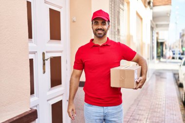 Genç İspanyol kurye sokakta paket tutuyor.