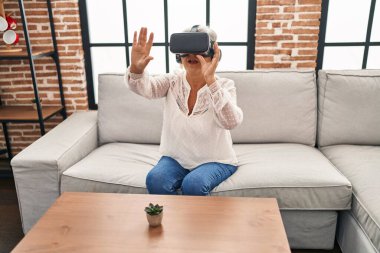 Evde sanal gerçeklik gözlüğü kullanan orta yaşlı bir kadın video oyunu oynuyor.