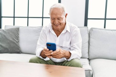 Kıdemli adam evde akıllı telefon kullanarak kendinden emin gülümsüyor.