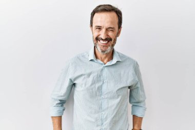 Middle age hispanic man with beard standing over isolated background winking looking at the camera with sexy expression, cheerful and happy face. 