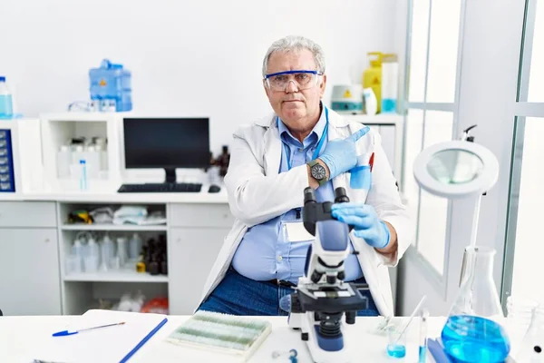 Senior caucasian man working at scientist laboratory pointing with hand finger to the side showing advertisement, serious and calm face