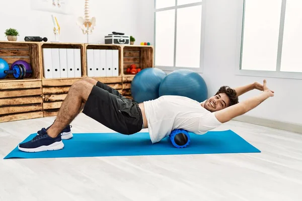 Genç İspanyol adam klinikte köpük silindiri kullanarak rehabilitasyon yapıyor.