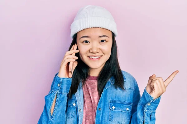 Молодая Китайская Девушка Разговаривает Смартфону Улыбаясь Счастливо Указывая Рукой Пальцем — стоковое фото