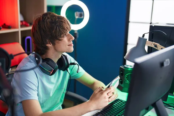 ゲームルームでコンピュータとスマートフォンを使用して若いブロンドの男ストリーマー — ストック写真