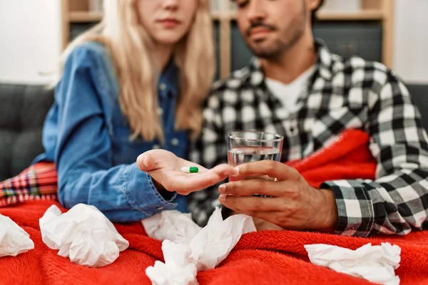 Young ill couple eating pills sitting on the sofa at home.