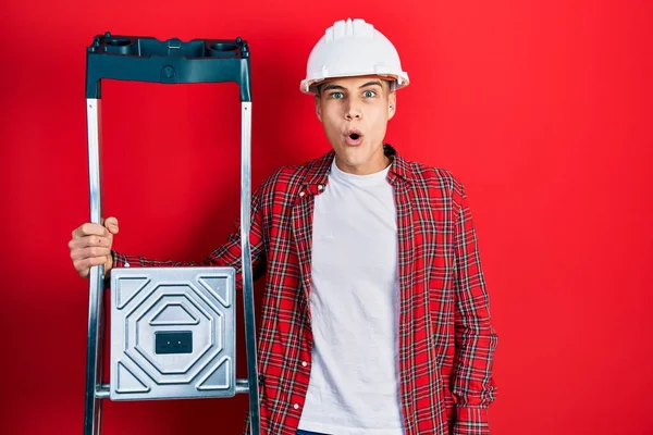 Young Hispanic Man Holding Construction Stairs Wearing Hardhat Scared Amazed — Stockfoto