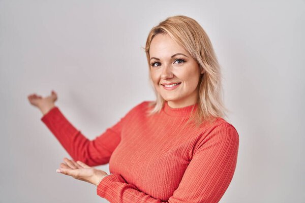 Blonde woman standing over isolated background inviting to enter smiling natural with open hand 