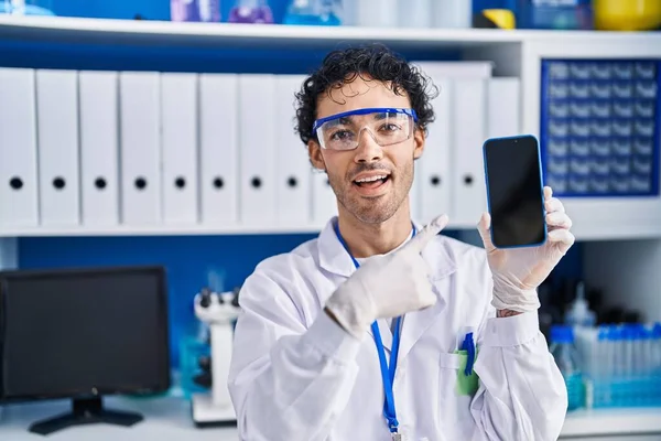 科学研究所で働くヒスパニック系の男を示していますスマートフォンの画面笑顔幸せなポインティングとともに手と指 — ストック写真