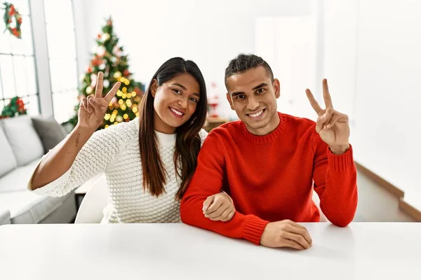 Jong Latijns Echtpaar Zit Tafel Door Kerstboom Glimlachend Naar Camera — Stockfoto