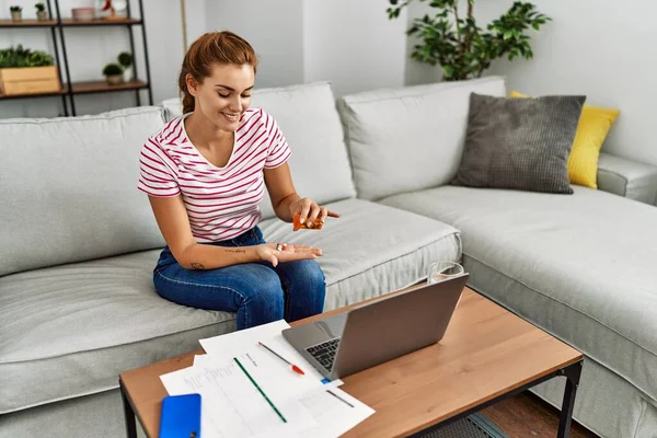 Haplar alan genç bir kadın çalışıyor ve evdeki kanepede oturuyor.