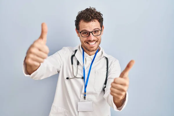 身穿医生制服和听诊器的年轻人 手握积极的手势 微笑着竖起大拇指 为成功感到高兴 优胜手势 — 图库照片