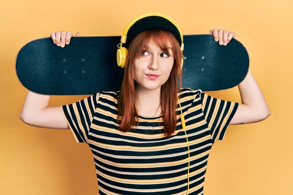 Redhead Young Woman Holding Skate Wearing Headphones Smiling Looking Side — Stock Photo, Image