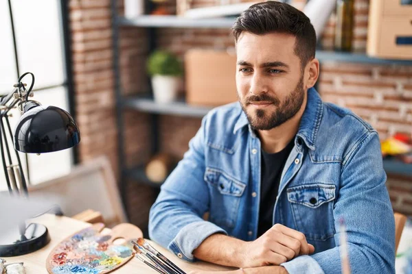 Masada oturan İspanyol genç adam sanat stüdyosunda kollarını kavuşturdu.