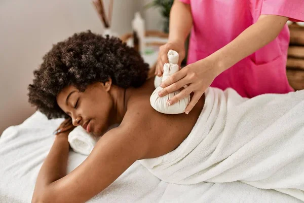 Genç Afrikalı Amerikalı kadın güzellik merkezinde Tayland çantalarıyla sırt masajı yaptırıyor.