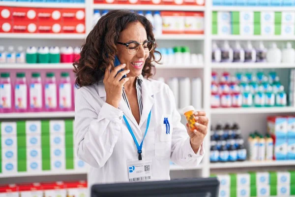 Middle Age Woman Pharmacist Holding Pills Bottle Talking Smartphone Pharmacy — Zdjęcie stockowe