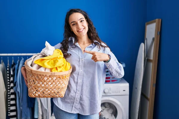 Ung Brunett Kvinna Håller Tvättkorg Ler Glad Pekar Med Hand — Stockfoto