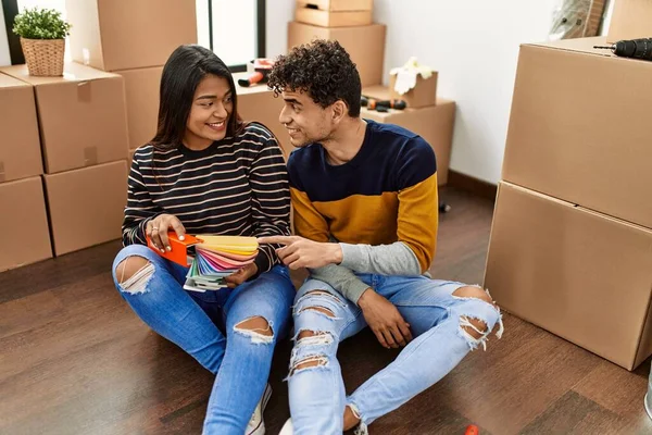 Young latin couple choosing paint color sitting on the floor at new home.