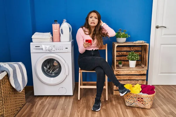 Genç İspanyol kadın çamaşırhane için bekliyor. Akıllı telefon kullanıyor. Deli ve korkmuş, korkmuş ve ağzı açık bir şekilde şok geçirmekten korkuyor. 