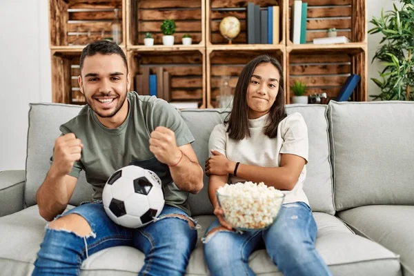 Genç latin çift evde futbol maçı izleyip porpcorn yiyorlar..