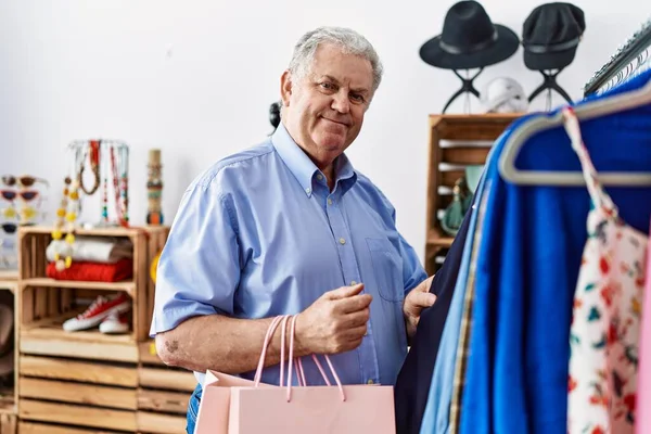 Orta yaşlı, gri saçlı, gülümseyen, kendine güvenen bir adam giyim mağazasından alışveriş yapıyor.