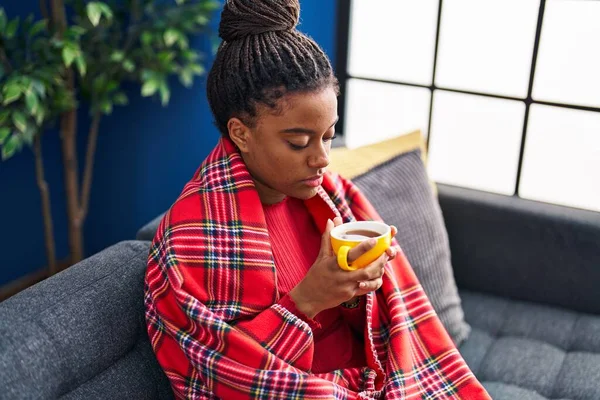African american woman drinking coffee sitting on sofa at home
