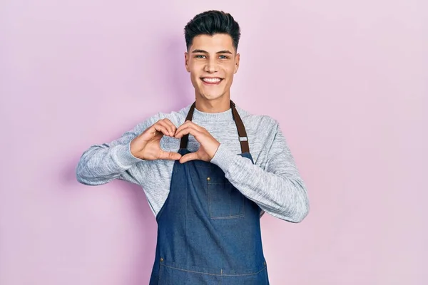 心のシンボルと手で形を示す愛に笑みを浮かべてエプロンを身に着けている若いヒスパニック系の男 ロマンチックなコンセプト — ストック写真
