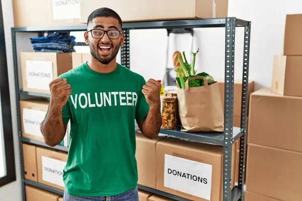 Young indian man volunteer holding donations box celebrating surprised and amazed for success with arms raised and open eyes. winner concept. 