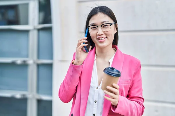 Chinese woman business worker talking on smartphone drinking coffee at street