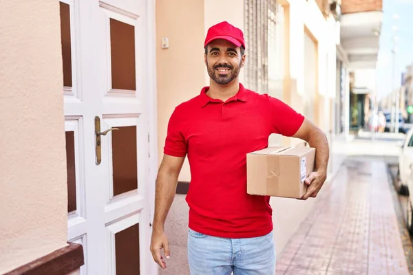 Genç İspanyol kurye sokakta paket tutuyor.