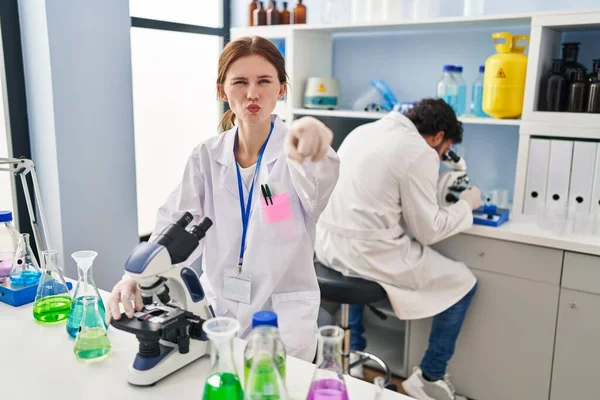 Young two people working at scientist laboratory pointing with finger to the camera and to you, confident gesture looking serious