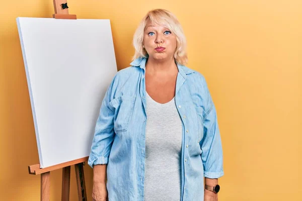 Middle Age Blonde Woman Standing Painter Easel Stand Puffing Cheeks — Fotografia de Stock