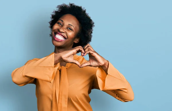 African american woman with afro hair wearing elegant shirt smiling in love showing heart symbol and shape with hands. romantic concept.