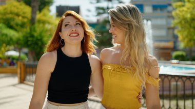 Two women hugging each other speaking and walking at park