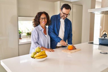 Orta yaşlı İspanyol çift gülümsüyor. Mutfakta turuncu kesiyorlar.