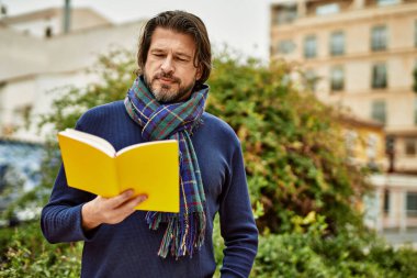 Orta yaşlı yakışıklı bir adam parkta kitap okuyor.