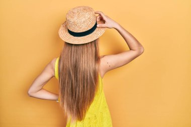 Sarışın kız, yaz şapkasını ters takmış, elleri kafasında şüpheyi düşünüyor. 