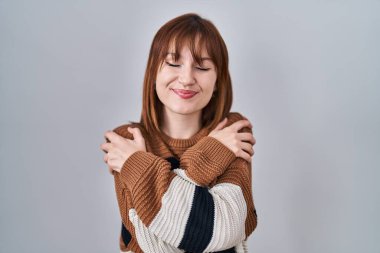 Soyutlanmış arka planda çizgili süveter giyen güzel bir kadın mutlu ve pozitif, kendinden emin gülümseyen bir şekilde kendine sarılıyor. Sevgi ve özgüven. 