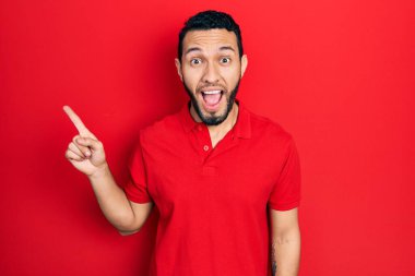 Hispanic man with beard pointing with fingers to the side celebrating crazy and amazed for success with open eyes screaming excited. 