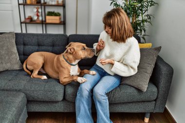 Beyaz kadın evdeki kanepede oturan köpeği besliyor.