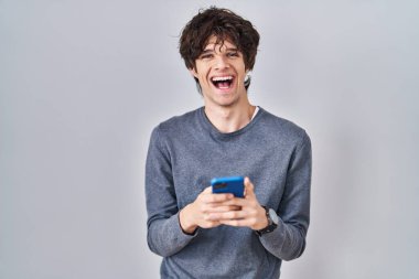 Genç adam akıllı telefon kullanıyor. Mesaj yazıyor. Gülümsüyor ve kahkahalar atıyor.. 