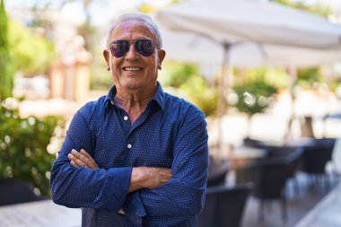 Senior grey-haired man smiling confident standing with arms crossed gesture at street