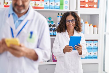 Man and woman pharmacists using touchpad and smartphone working at pharmacy