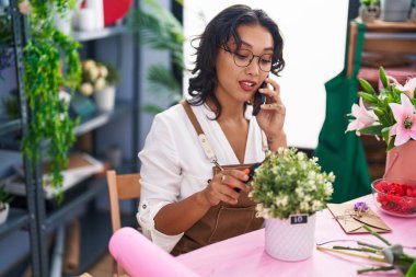 Çiçekçide akıllı telefondan konuşan güzel İspanyol kadın çiçekçi.