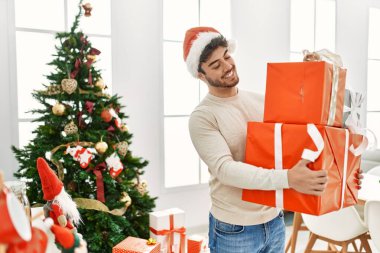 Genç İspanyol adam gülümseyerek mutlu bir şekilde evde hediyeler tutuyor..