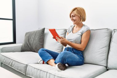 Orta yaşlı sarışın kadın evde dokunmatik ped kullanarak gülümsüyor.