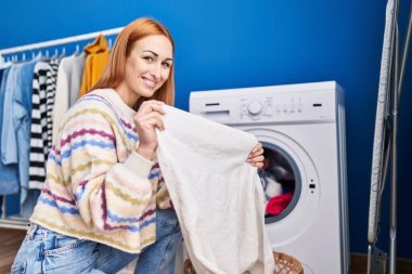 Çamaşır odasında kendine güvenen beyaz bir kadın gülümsüyor.