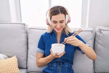 Young woman listening to music eating chinese food at home